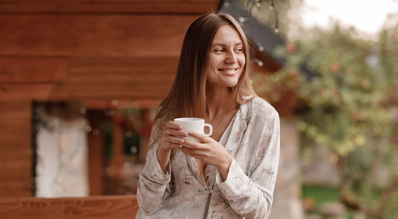 Is green tea acidic with Woman holding a cup of green tea standing at the balcony overlooking the garden