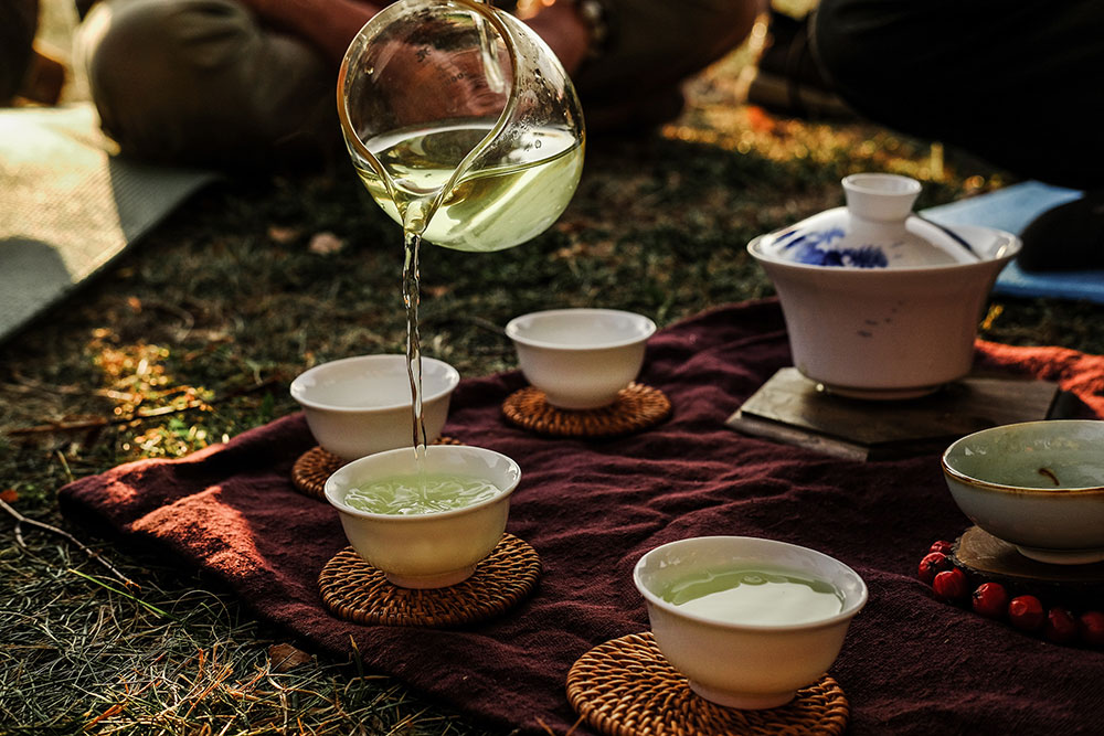 Pouring green tea into tea cups from a glass flask