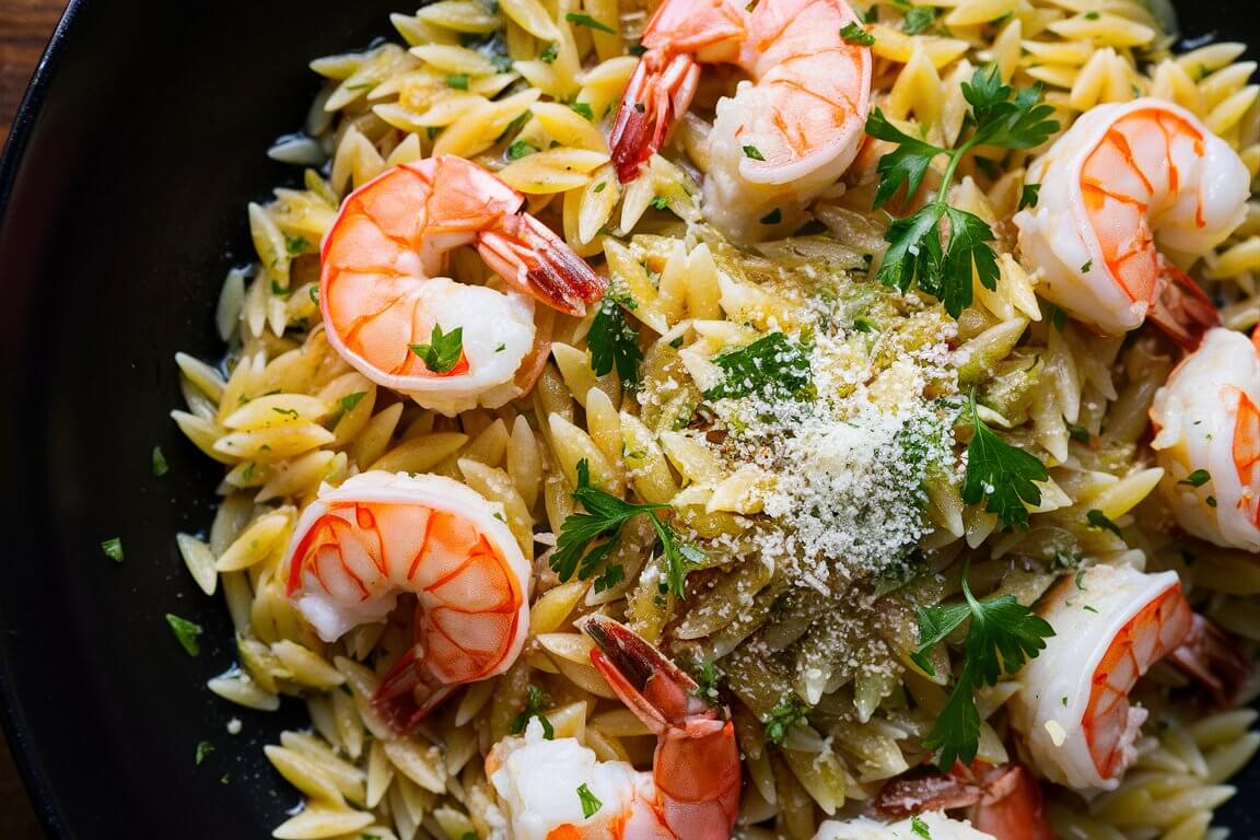 Orzo pasta with shrimp, garnished with parsley and grated cheese, served on a black plate. Appealing and appetizing close-up food presentation.