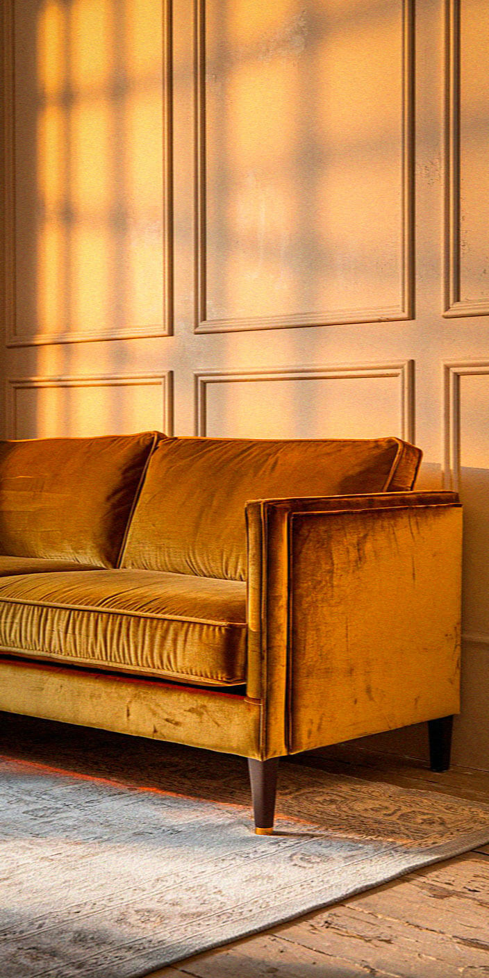 A cozy room with a mustard sofa, soft rug, and paneled wall bathed in warm sunlight, creates an inviting, serene atmosphere.