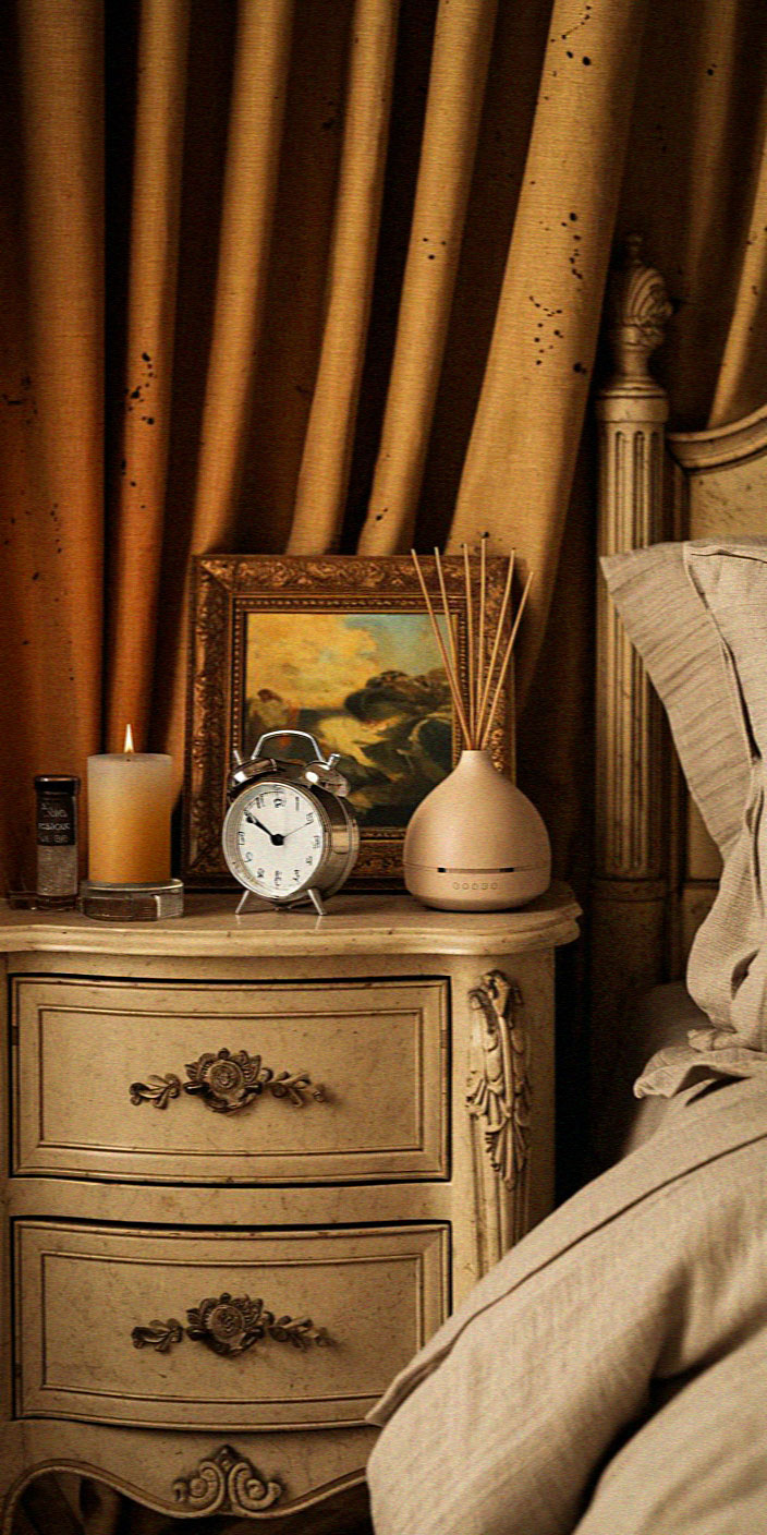 Vintage bedside table with ornate designs, clock, candle, diffuser, and framed painting. Luxurious drapery in the background adds warmth and elegance.