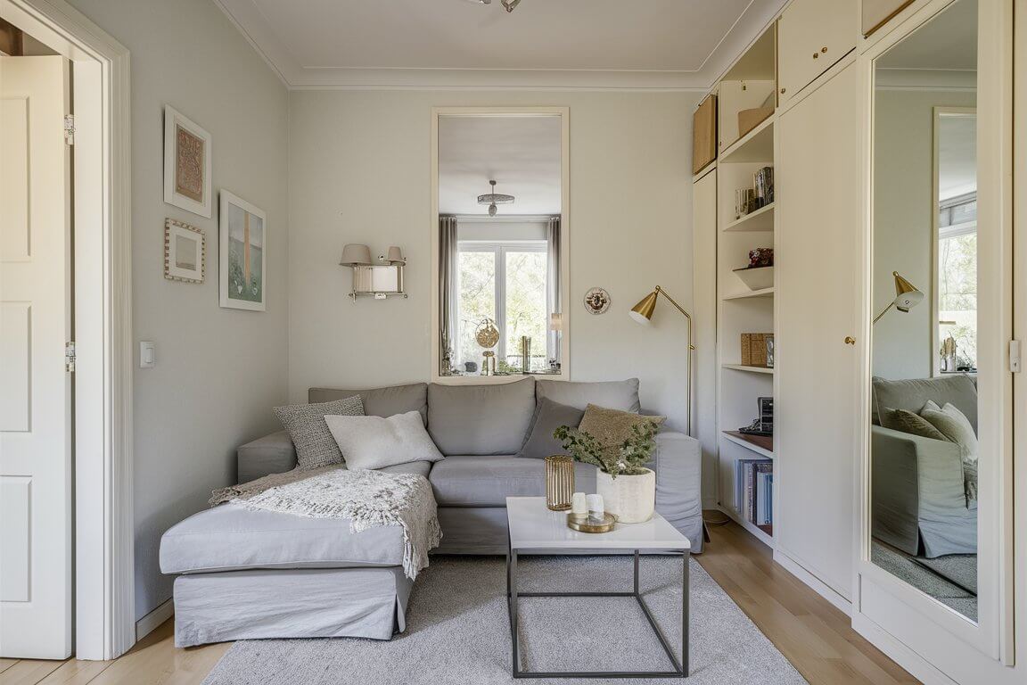 Cozy living room with gray sectional sofa, coffee table, and decorative artwork. Built-in bookshelves and large mirror enhance the airy, modern space.
