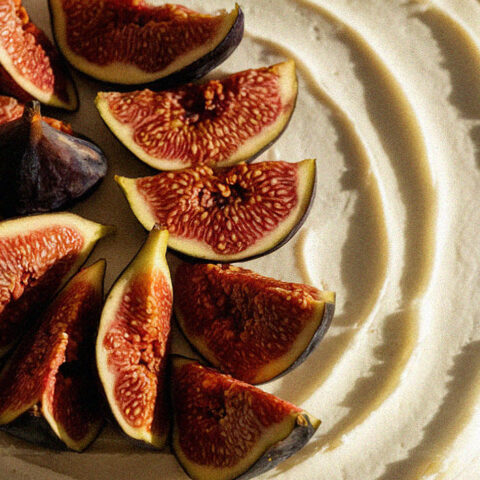 A fig-topped tart on a golden crust, with creamy filling, beautifully catches the light, highlighting texture and freshness in a simple, elegant presentation.