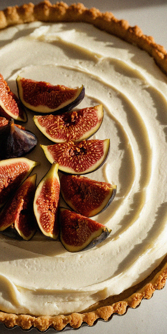 A fig-topped tart on a golden crust, with creamy filling, beautifully catches the light, highlighting texture and freshness in a simple, elegant presentation.