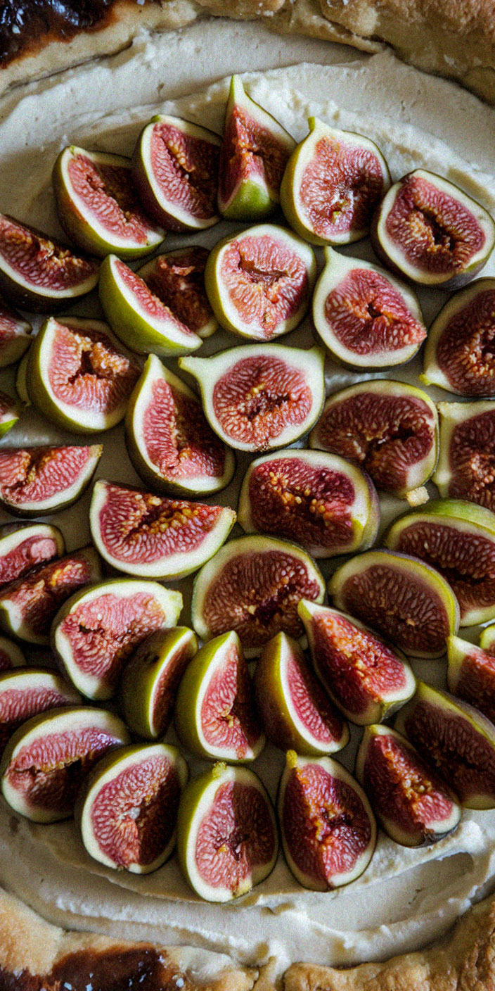 A tart topped with sliced figs arranged on creamy filling, surrounded by golden-brown crust. The figs display vibrant green and pink hues.