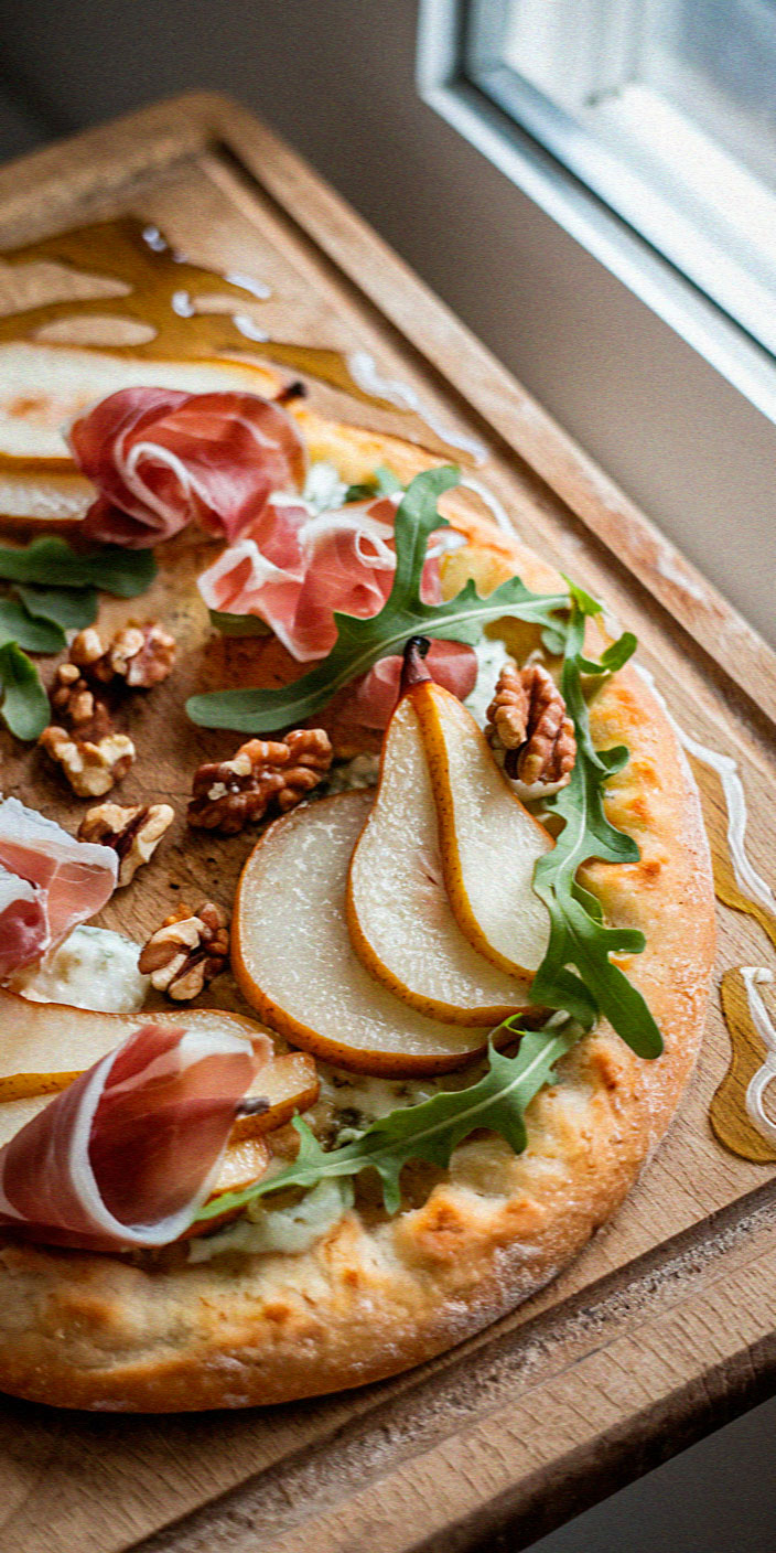 Gourmet pizza topped with prosciutto, pear slices, walnuts, arugula, and drizzled with honey on a wooden board near a window.
