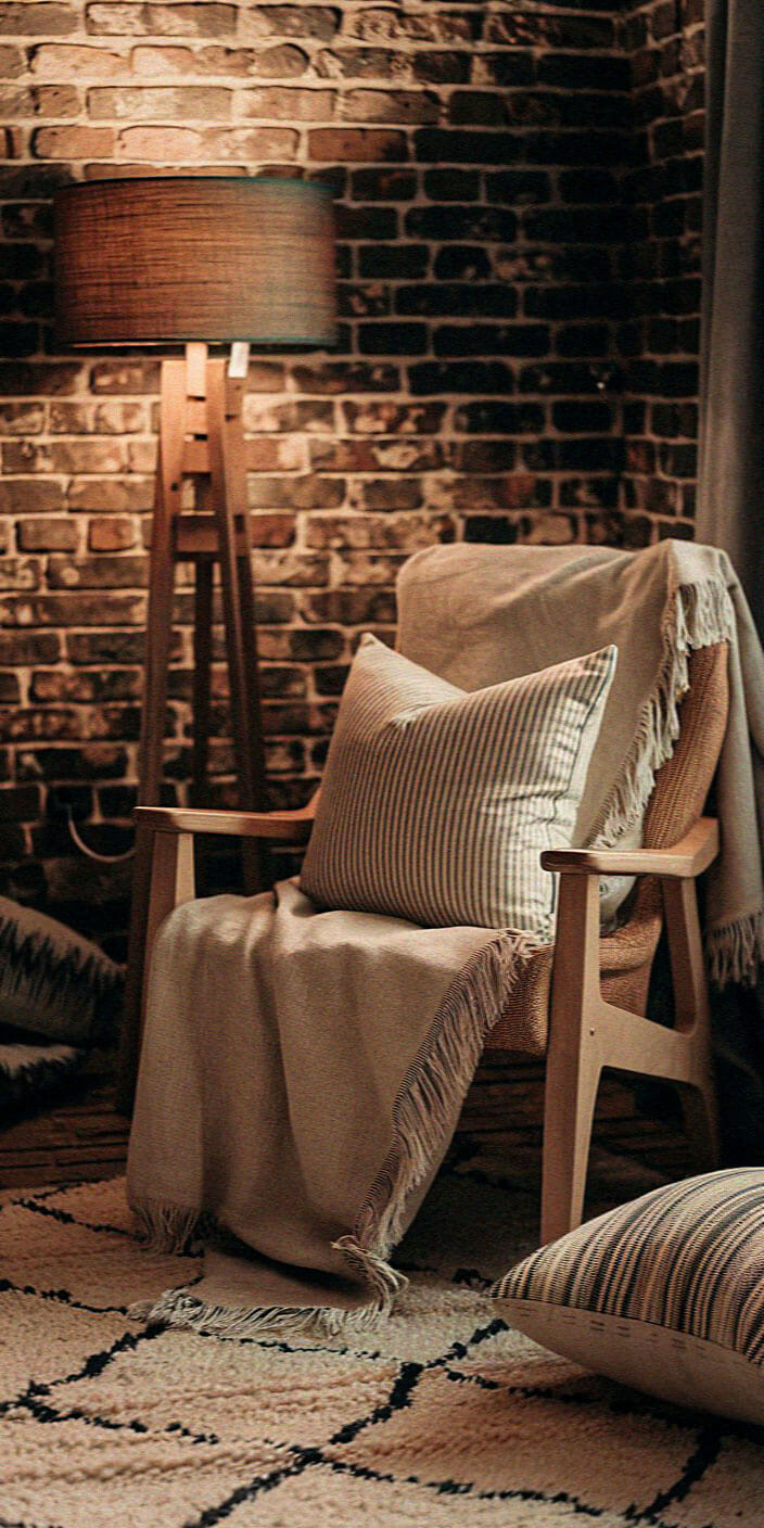 Cozy room with a wooden chair, striped cushion, and lamp against a brick wall. Soft lighting creates a warm, inviting atmosphere.
