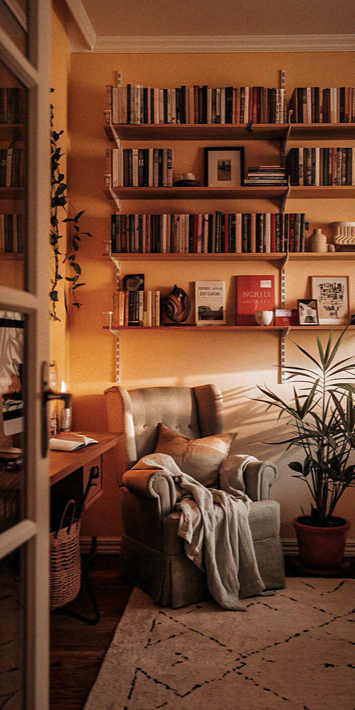 Cozy room with a soft armchair, vibrant bookshelves, and a warm-toned lamp, creating an inviting reading nook atmosphere with natural light.