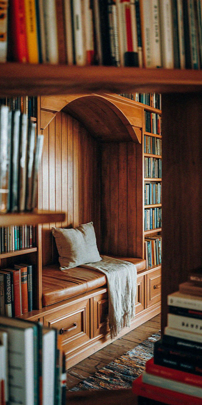 Cozy wooden nook with integrated bookshelves and seating, adorned with books and a cushion, providing a warm, inviting reading spot.
