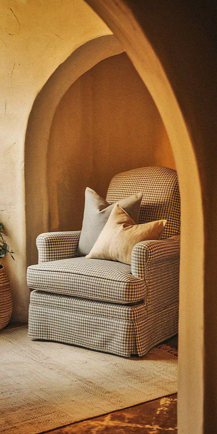 Cozy room with an upholstered armchair featuring plaid fabric and cushions, framed by an architectural arch, creating a warm and inviting atmosphere.