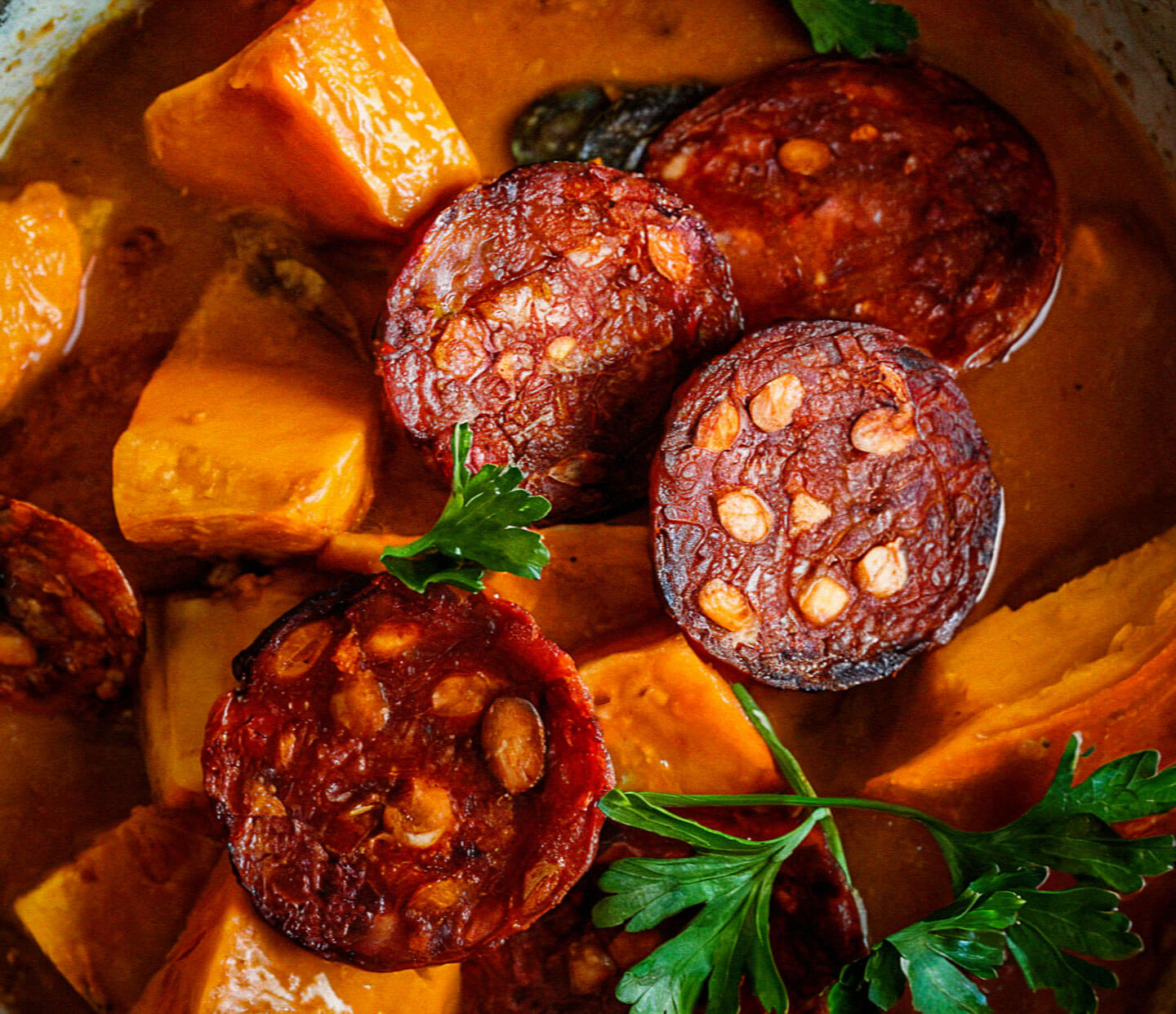 Slices of spicy sausage with chunks of squash in a rich, savory sauce, garnished with fresh parsley leaves for an appetizing presentation.