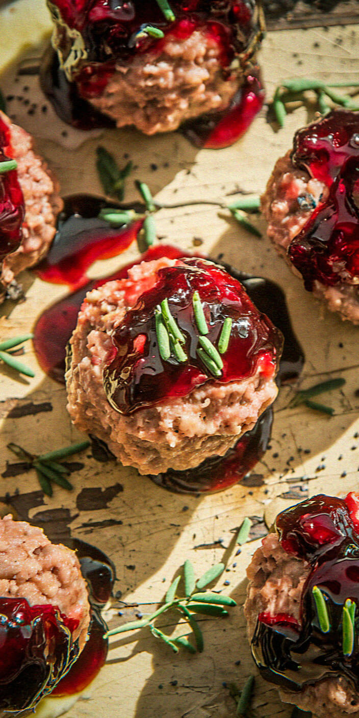 Close-up of savory hors d'oeuvres topped with rich red sauce and garnished with fresh herbs, arranged on a textured, light-colored surface.