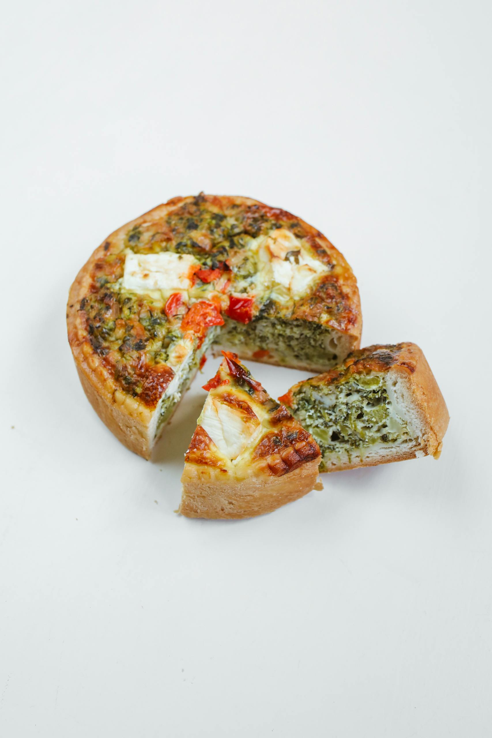 A savory spinach and feta quiche with vegetables, captured in a vertical shot on a white background.