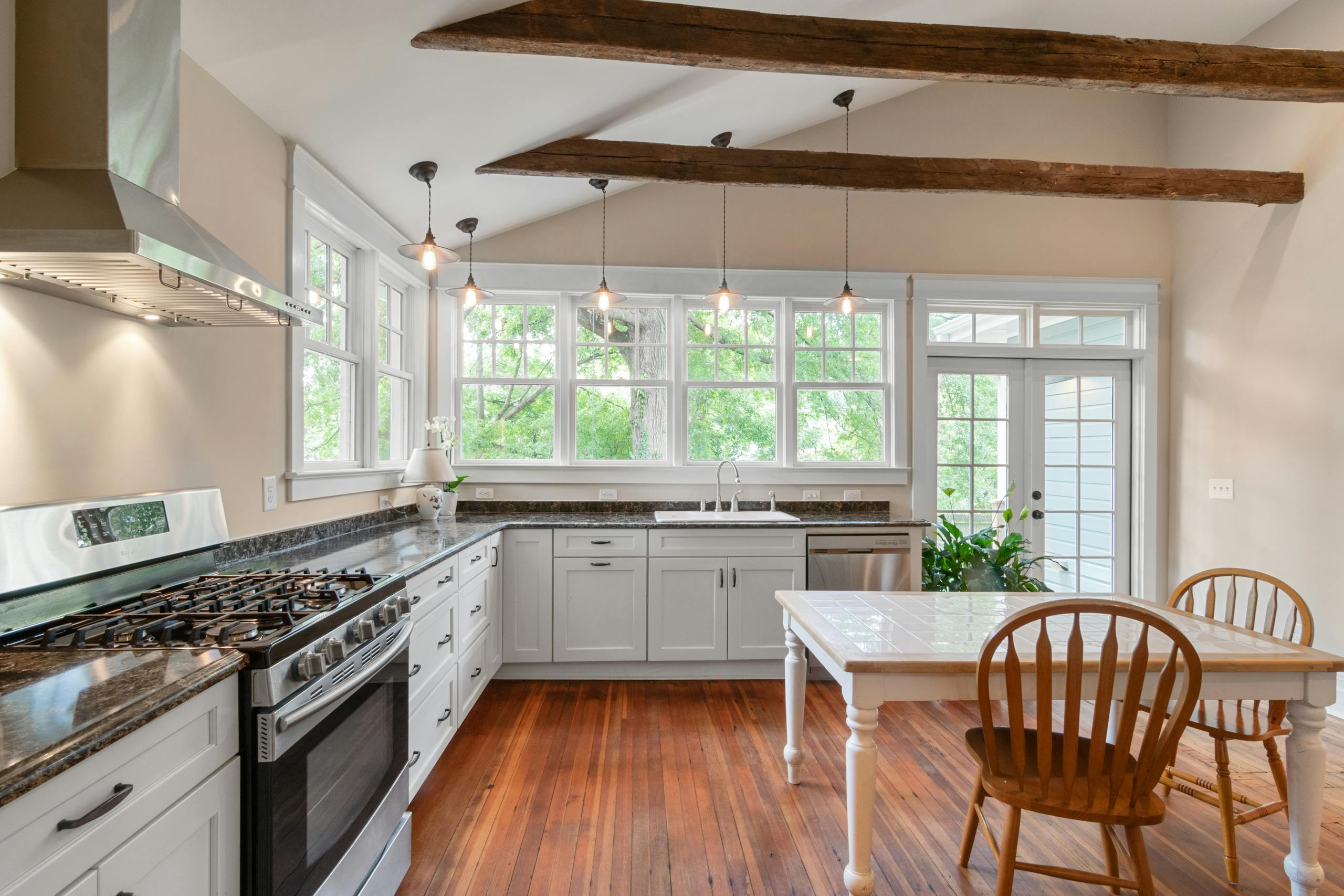 Bright kitchen interior featuring wooden beams, white cabinetry, and natural lighting.