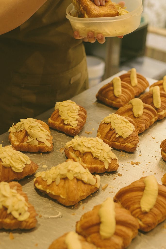 Close-up of fresh almond croissants being prepared by a bakery chef.