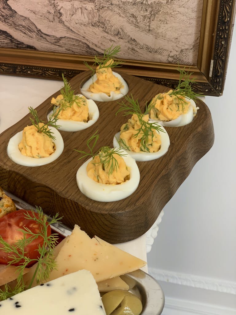 Close-up of garnished deviled eggs on a wooden platter with cheese and tomato slices.