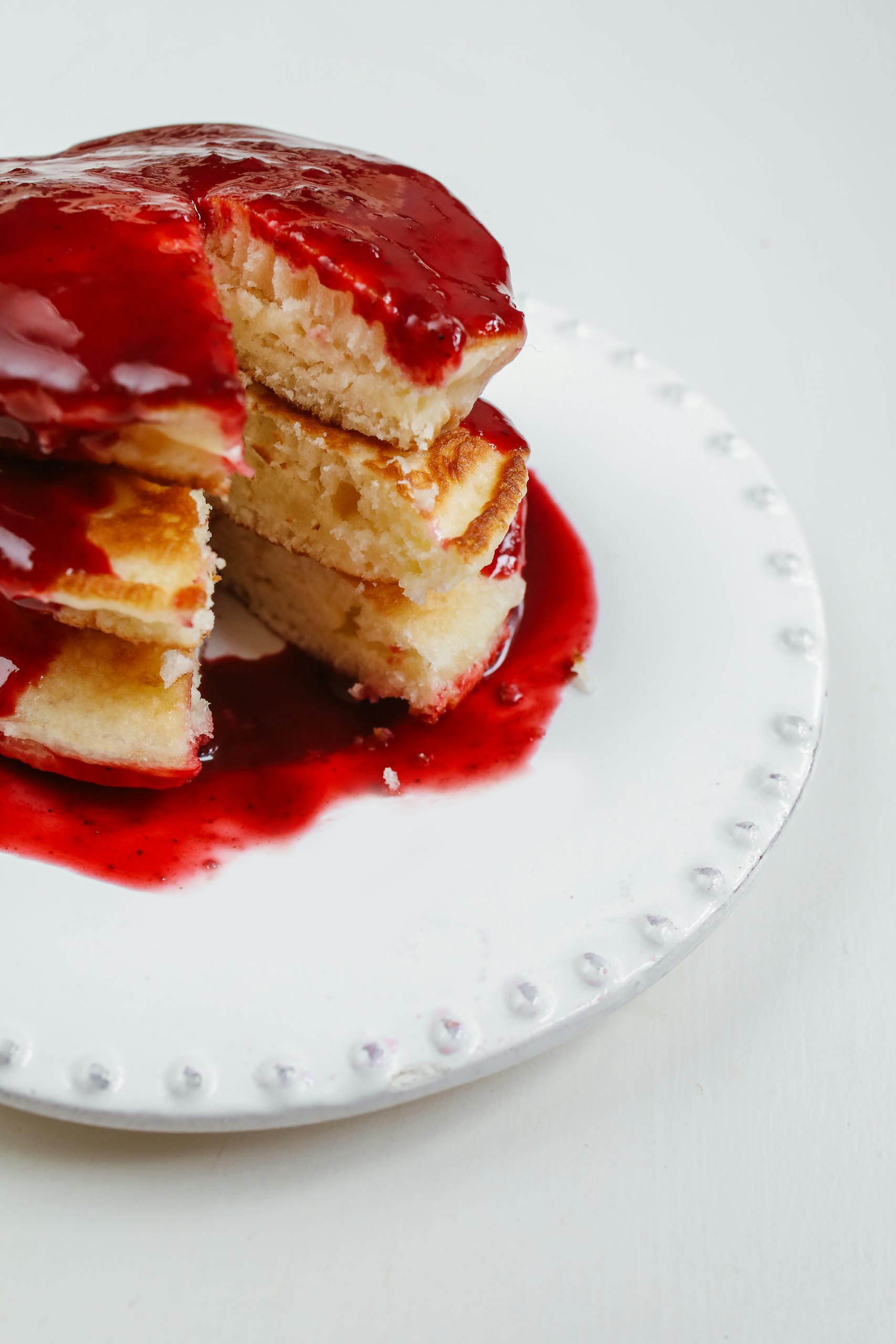 Delicious pancakes drizzled with strawberry syrup on a white ceramic plate.