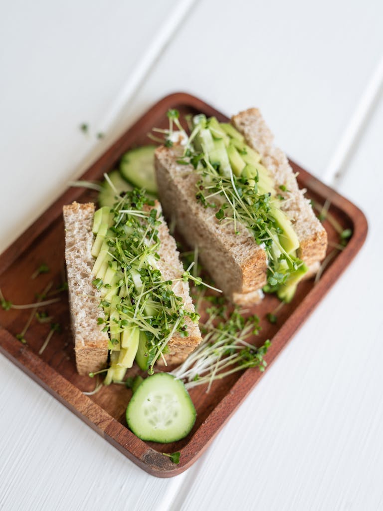 Delicious vegetable sandwich with cucumber and sprouts on a wooden plate.
