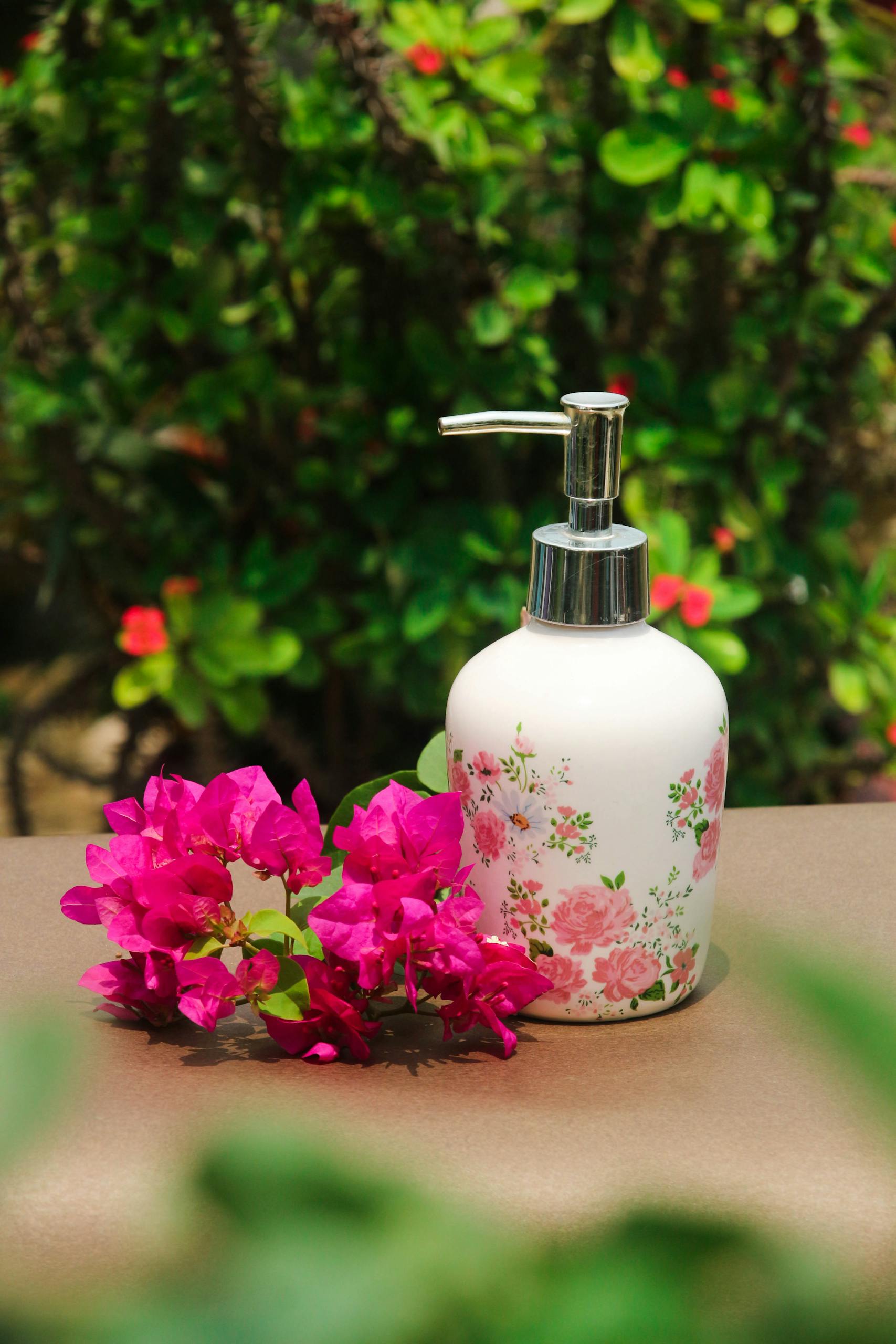 Elegant soap dispenser with floral design surrounded by vibrant pink bougainvillea flowers outdoors.