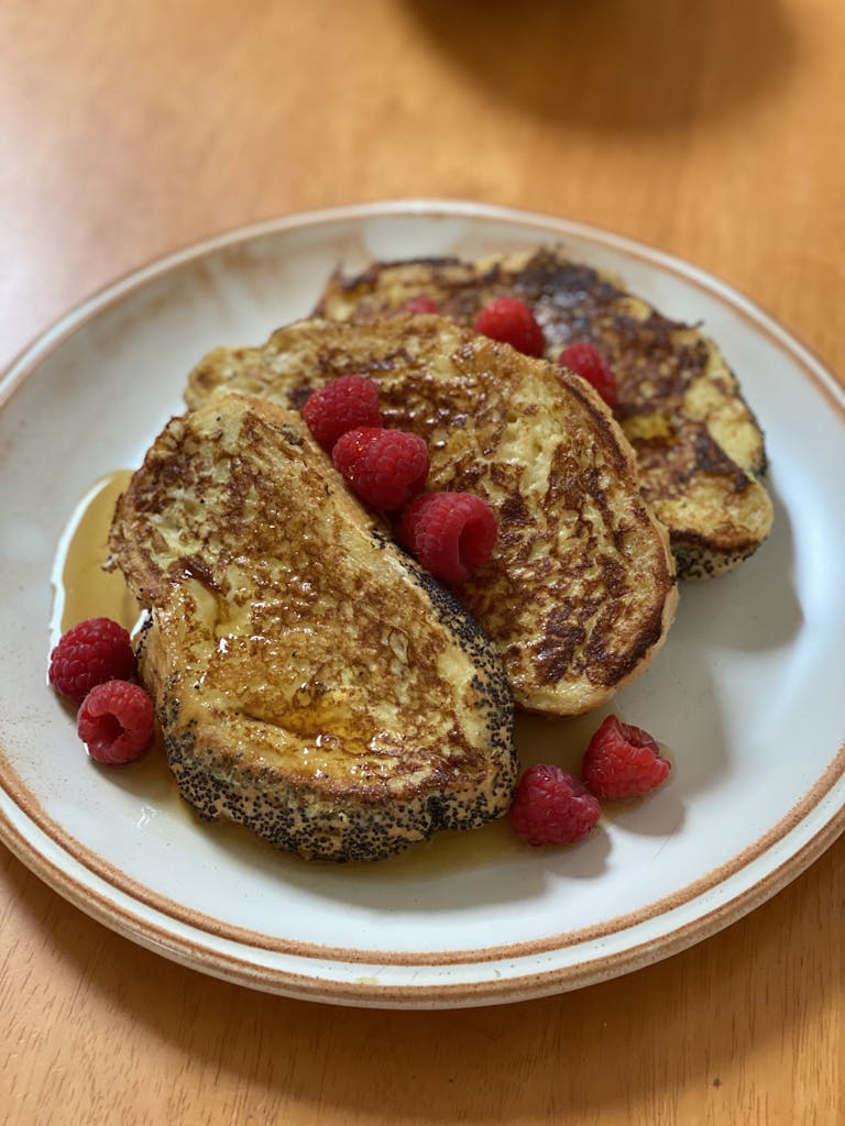 Golden-brown french toast topped with fresh raspberries and drizzled with syrup on a plate.