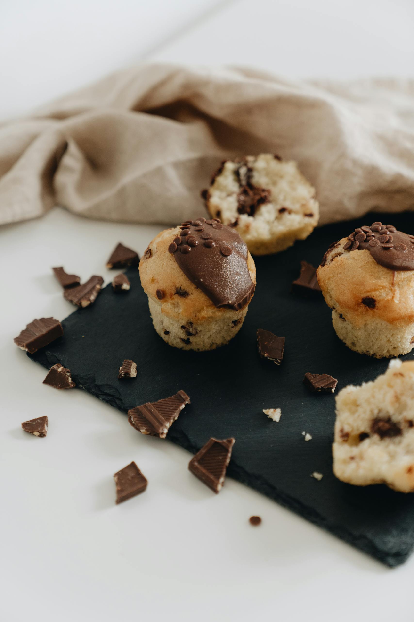 Indulge in delightful chocolate chip muffins, beautifully styled on a dark slate surface with scattered chocolate pieces.