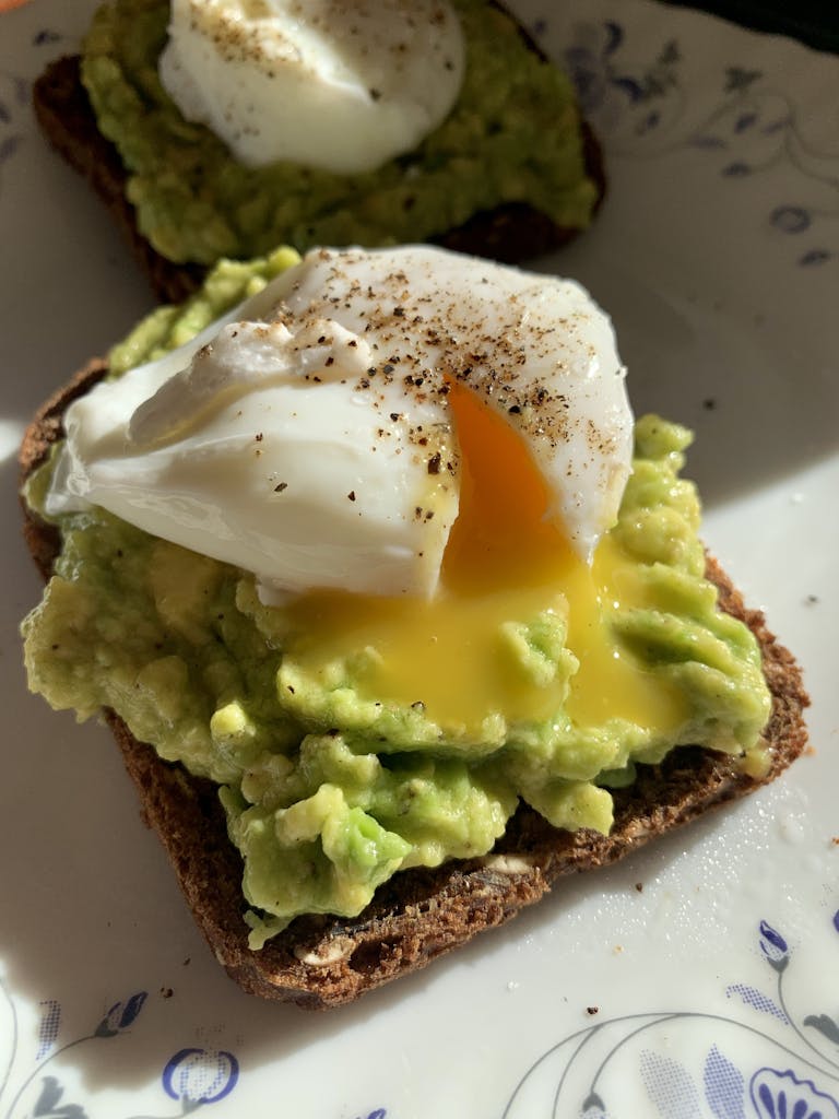 Savory avocado toast topped with a perfectly poached egg and seasoned with pepper.