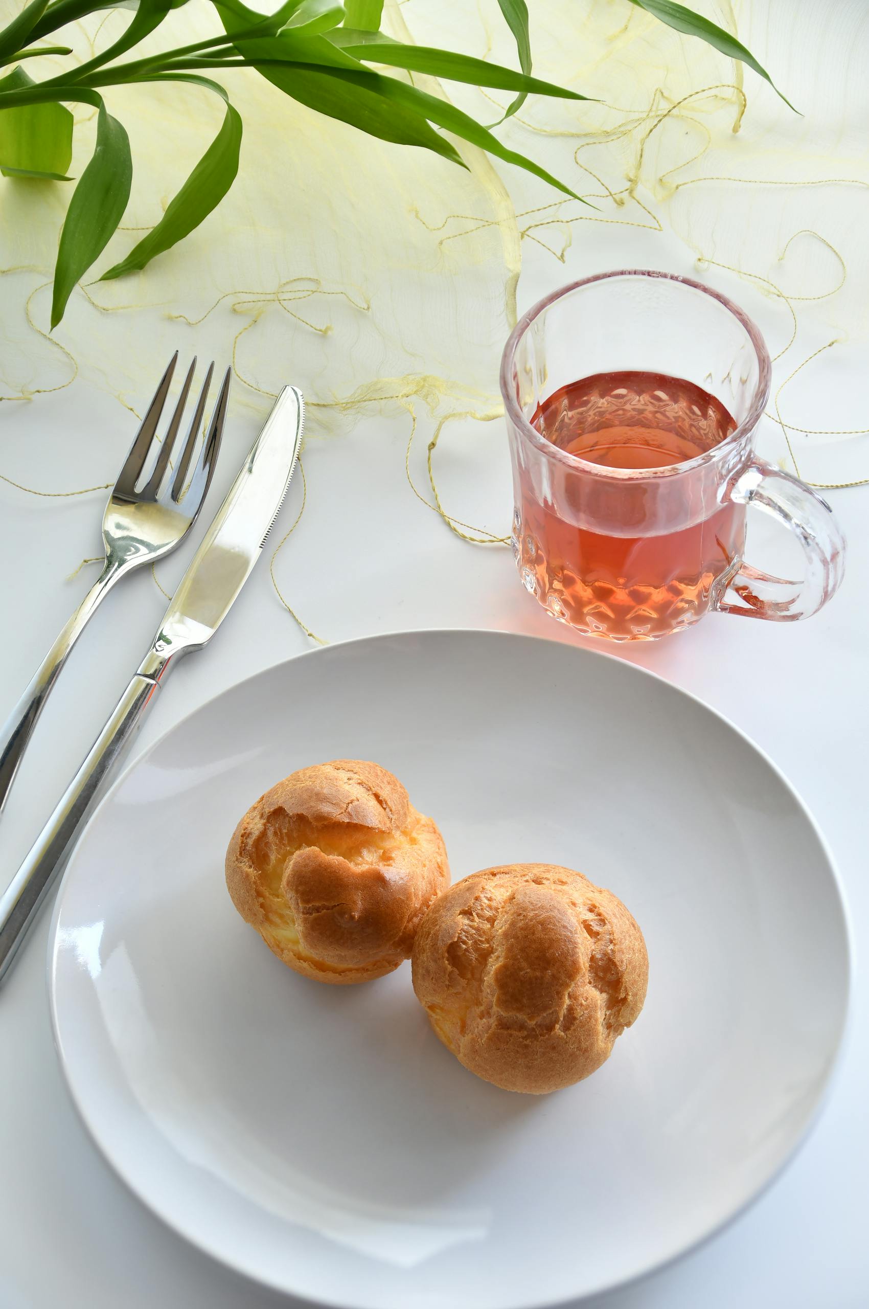 Tasty cream puffs served with a glass of black tea on a white plate, photographed in an elegant setting.
