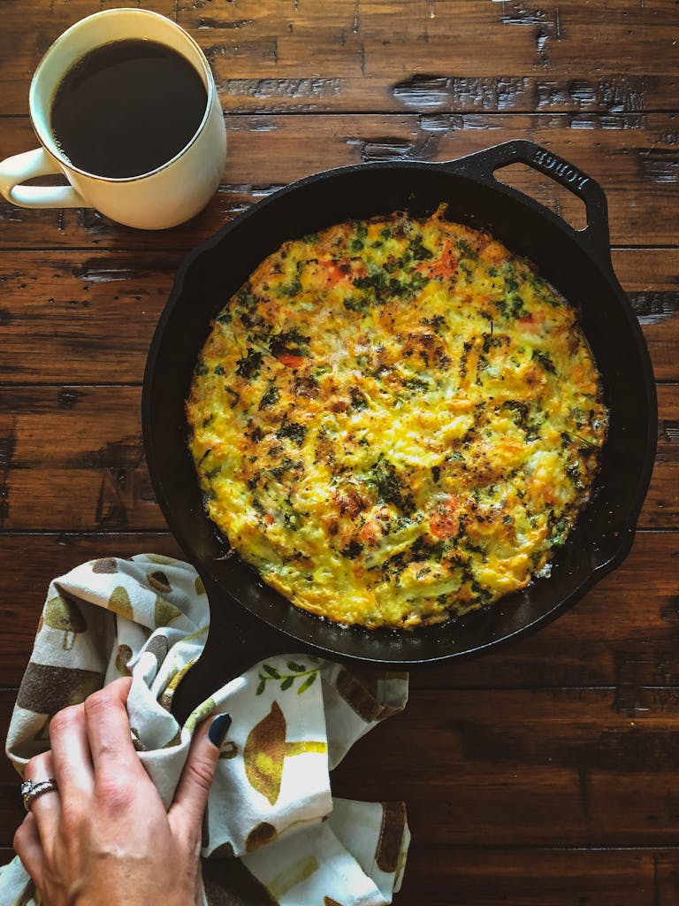 Tasty vegetable frittata in a cast iron skillet with coffee on a wooden table.