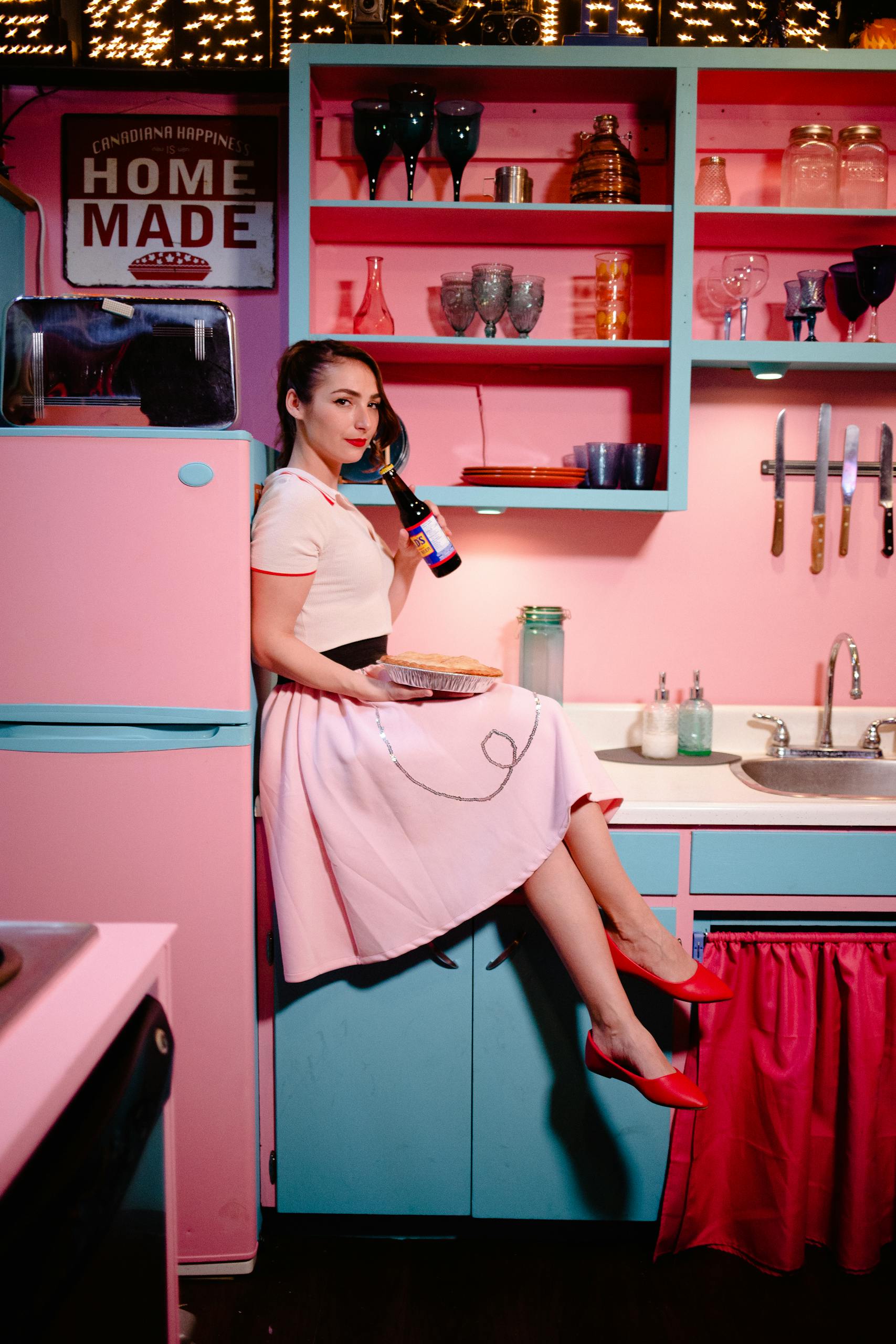 Woman in a vintage pink kitchen wearing a retro dress, embodies classic 50s style.