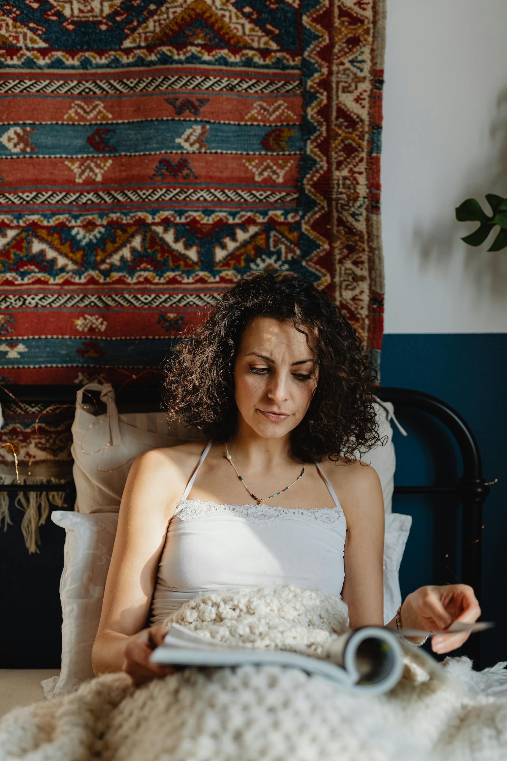 A woman enjoys a book while relaxing in a beautifully decorated bohemian bedroom.