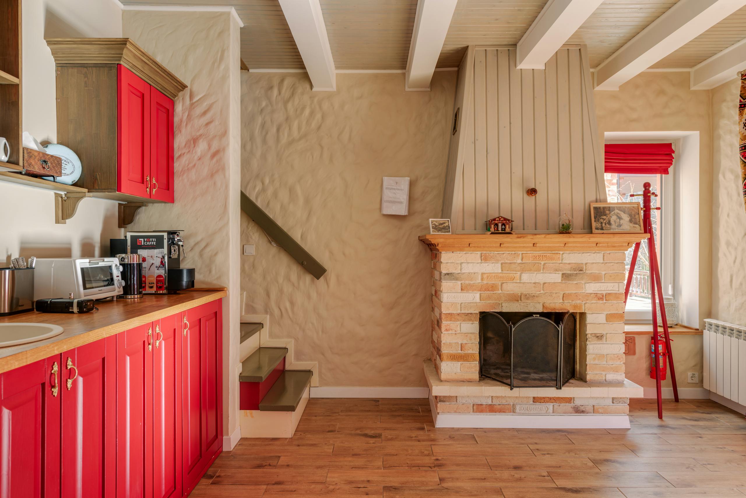 Warm rustic kitchen interior with vibrant red cabinets and a charming brick fireplace for a cozy home feel.