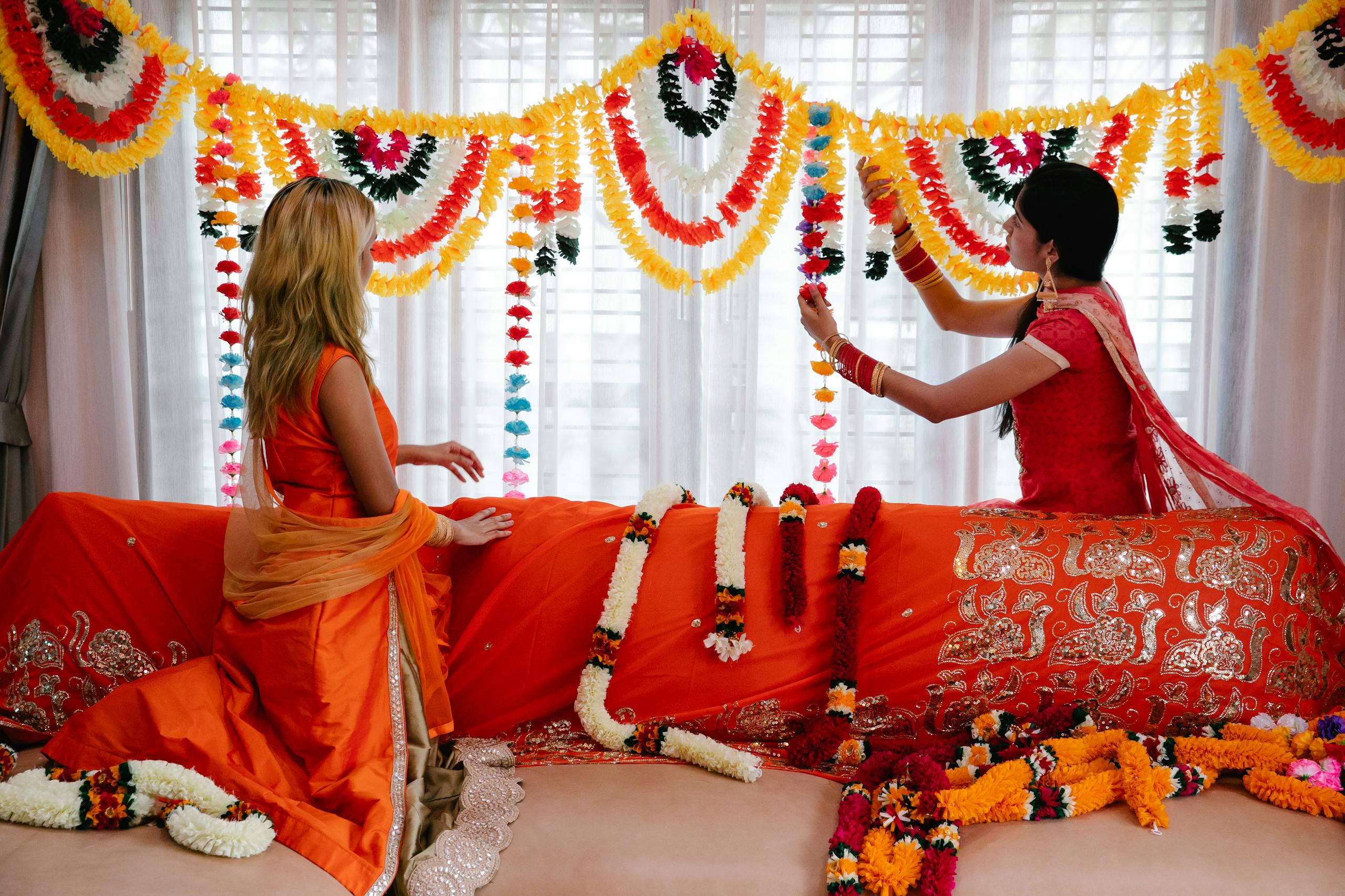 Women decorating indoors with vibrant flower garlands for a traditional Indian celebration.