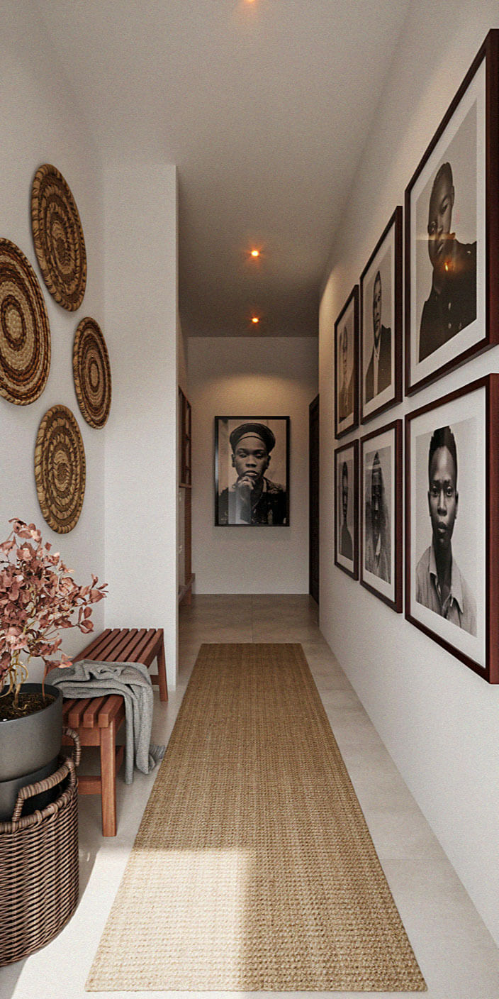 Bright hallway with framed portraits along the right wall, circular woven wall art on the left, a potted plant and woven baskets by a small table, and a beige runner rug leading to a large portrait at the far end.