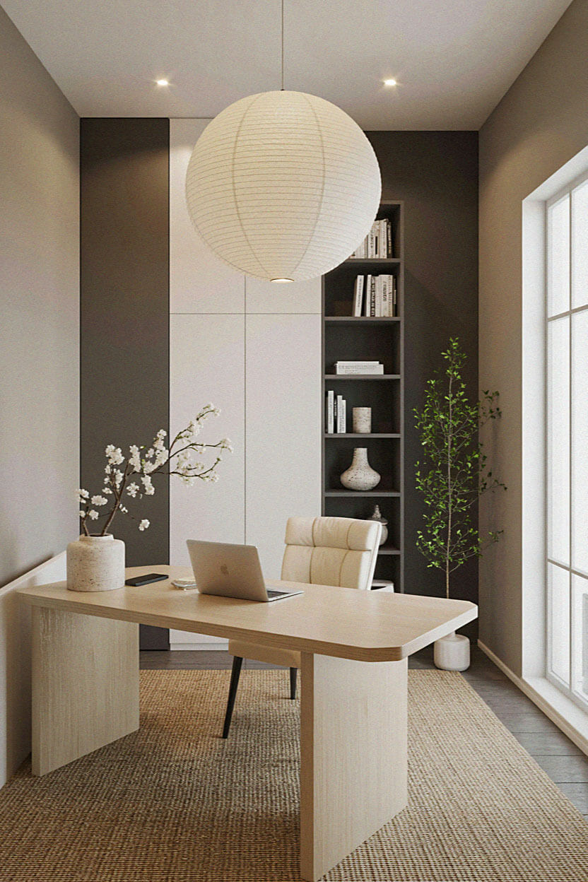 Minimalist home office with a wooden desk, a white paper lantern pendant light, a laptop, beige chair, a tall bookshelf, and a large window letting in natural light.